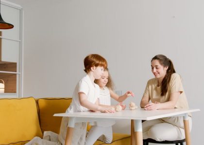 A mother and two children playing blocks on a white table in a cozy living room.